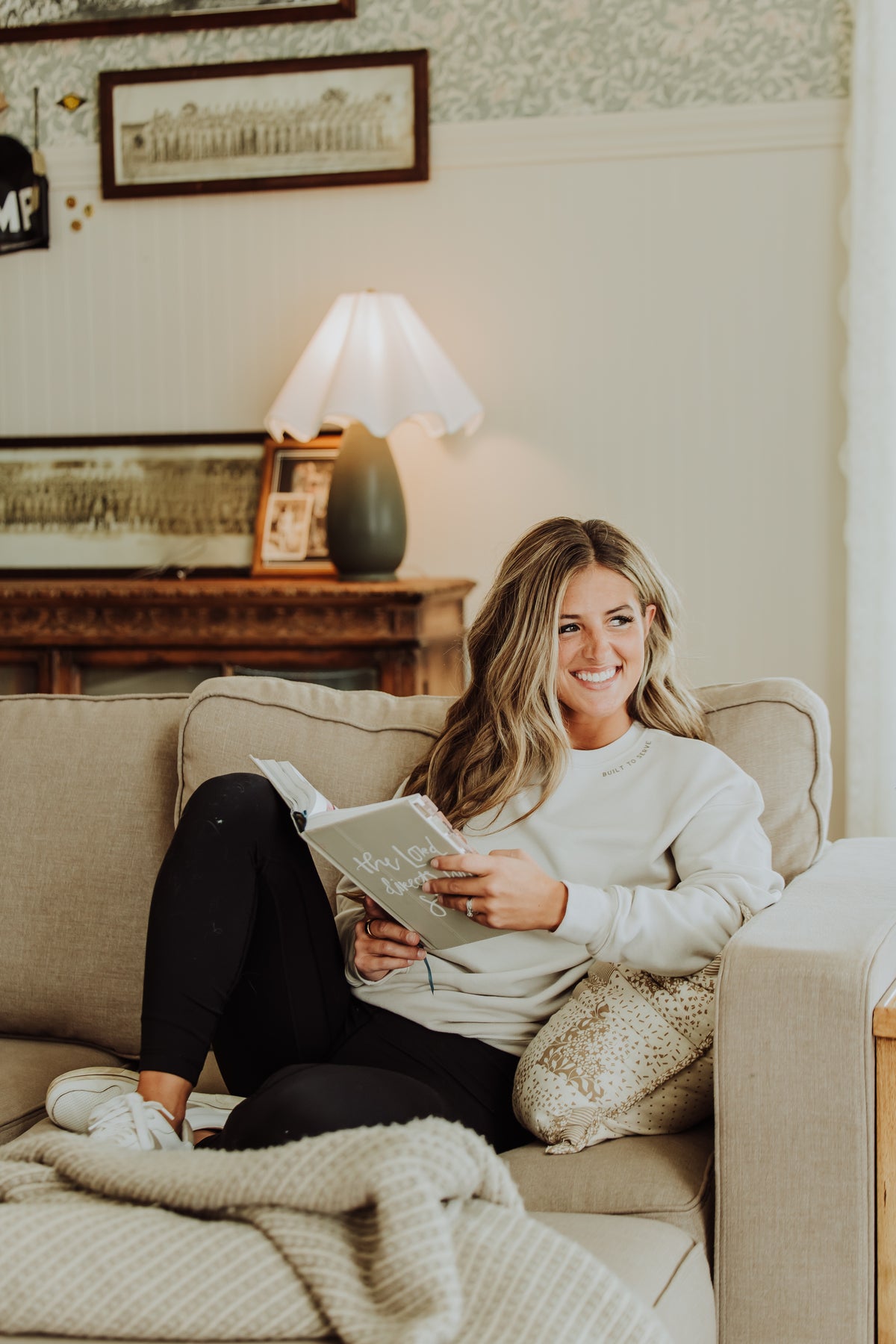 Woman sitting on a couch reading a book in a cozy living room.