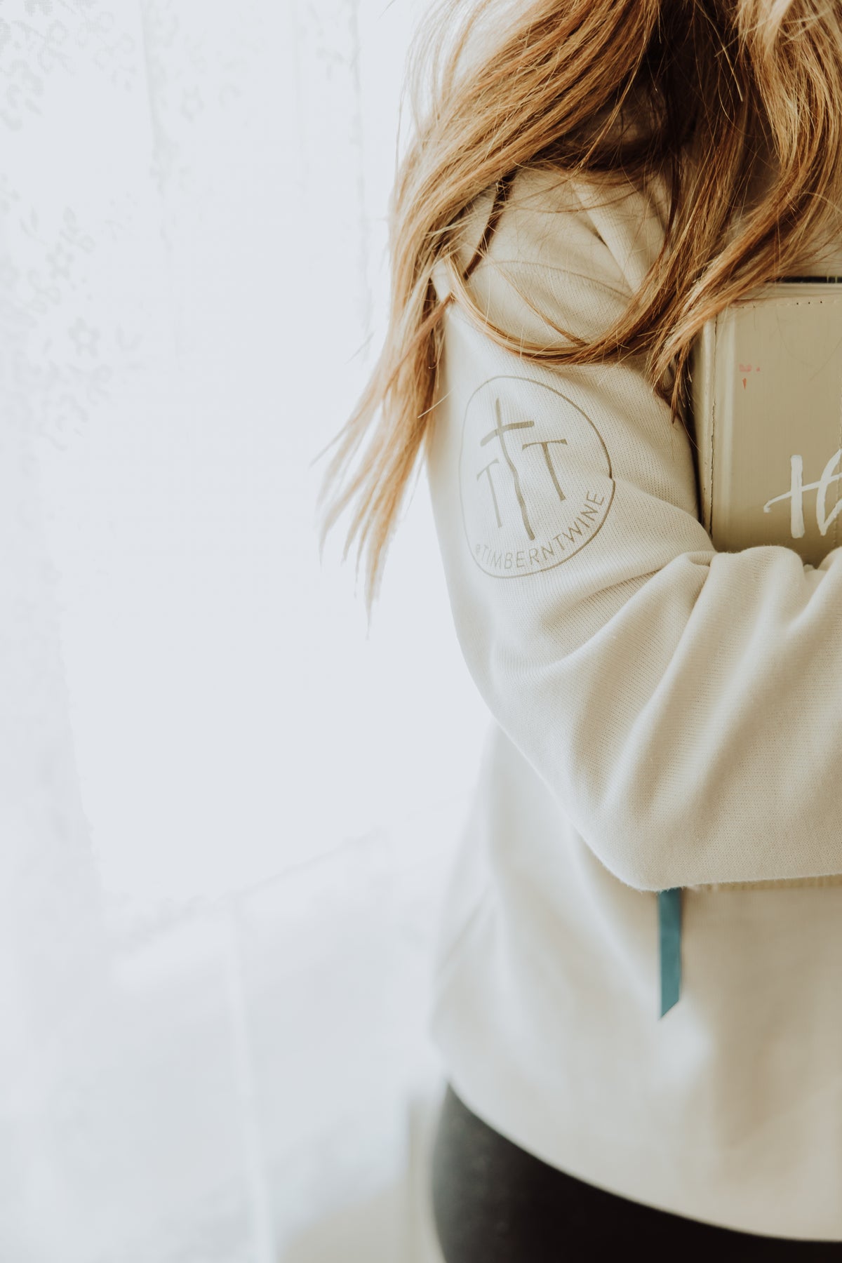 Person wearing a beige hoodie with a logo on the sleeve against a white background