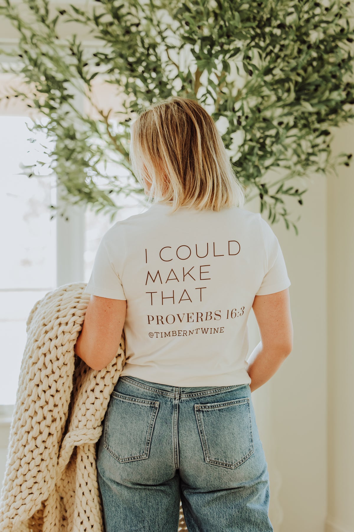 Person wearing a t-shirt with text, standing in front of greenery