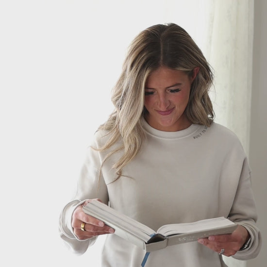 woman against a white background holding a book wearing a sweatshirt